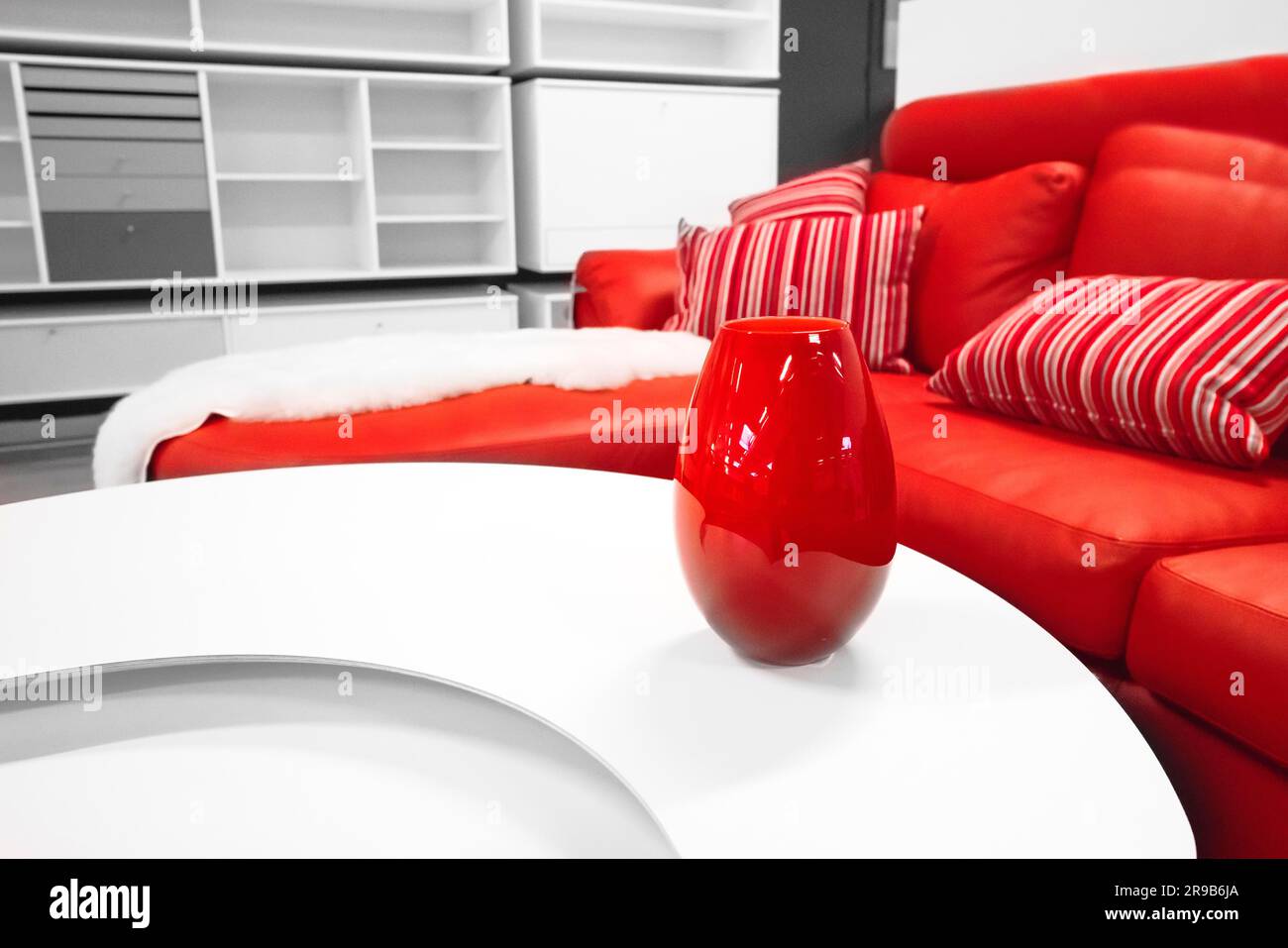 Red vase on a table in a stylish living room with a red couch with decorative pillows in white colors Stock Photo