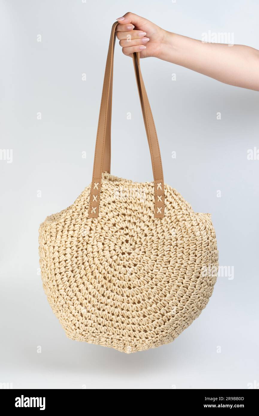 Round beige color straw bag hang on hand isolated Stock Photo