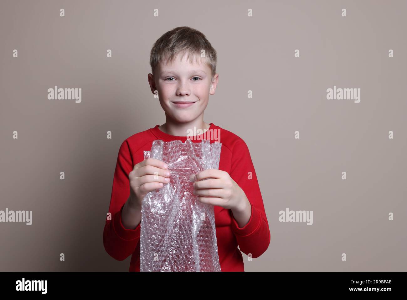 Boy popping bubble wrap on beige background. Stress relief Stock Photo