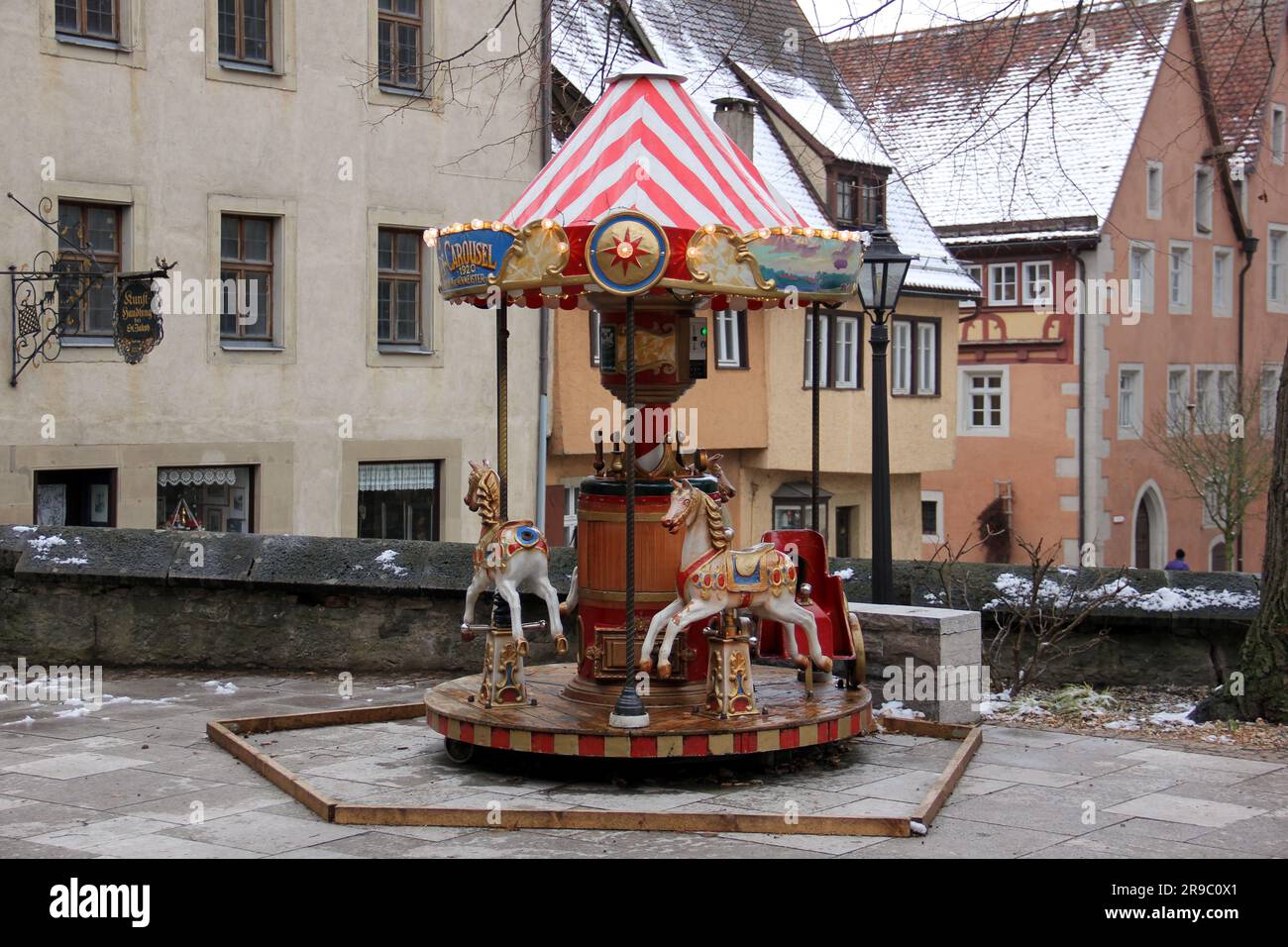 Old-times styled merry-go-round in the small square in the old town, snow covered gable roofed townhouses in the background, Rothenburg ob der Tauber Stock Photo