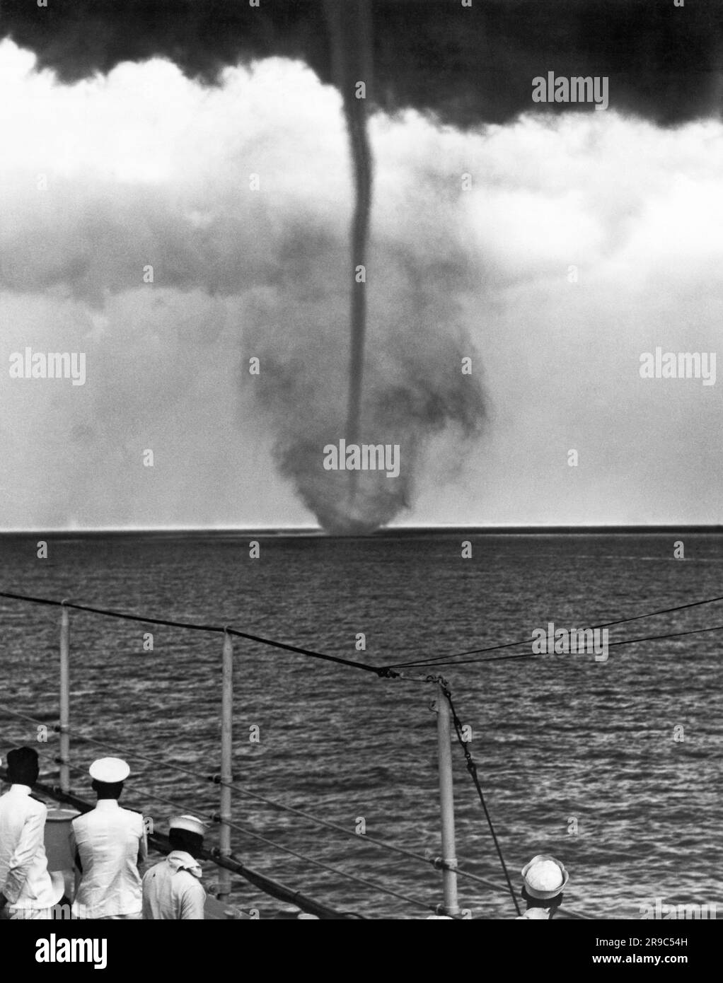 China:  c. 1930 Sailors aboard the U.S.S. Pittsburgh watch a waterspout that has formed by the mouth of the Yangtze River. Stock Photo