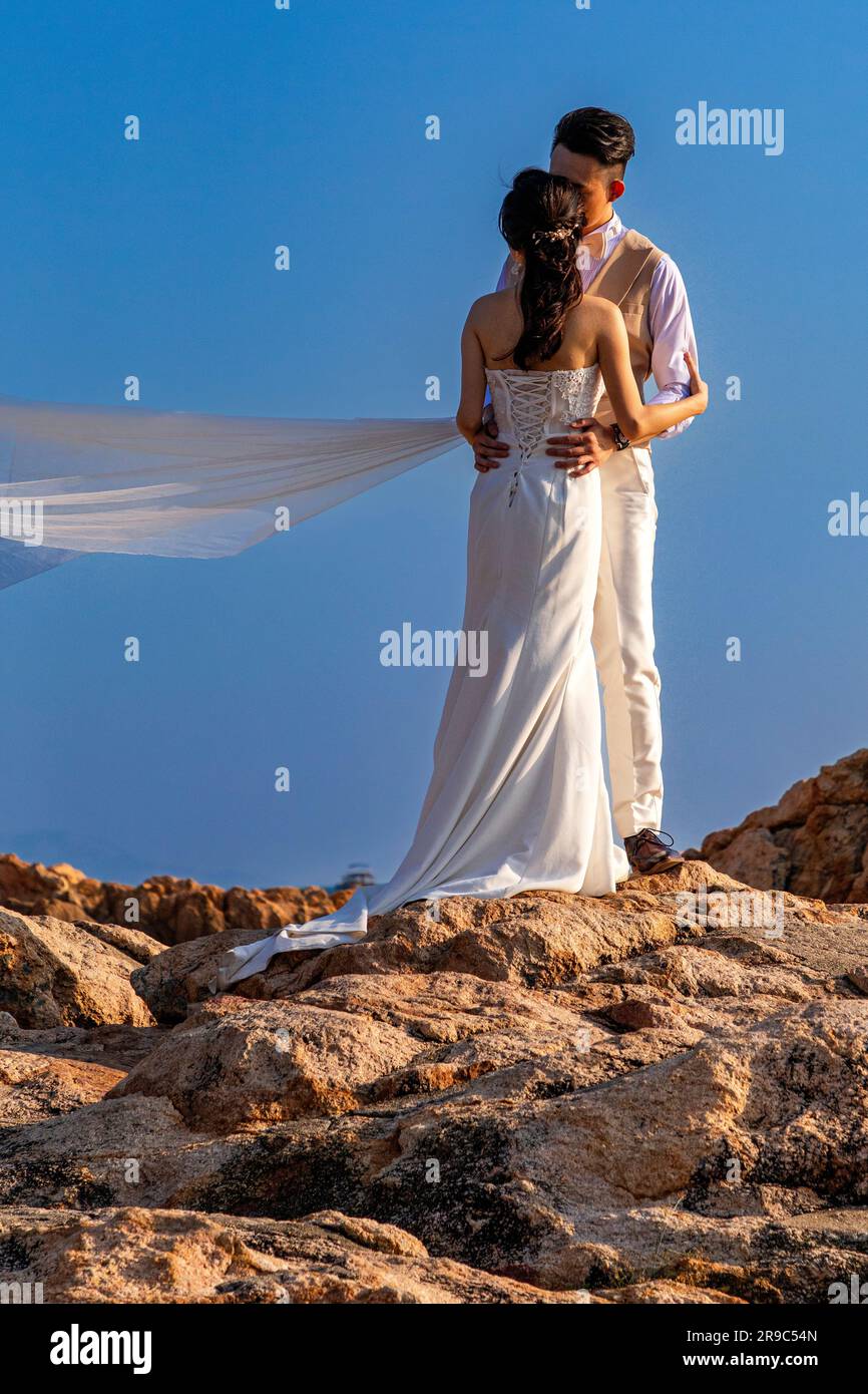 Young Chinese couple posing for wedding photographs on rocks, Stanley harbour, Hong Kong, SAR, China Stock Photo