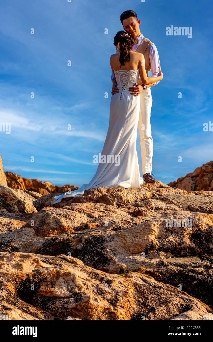 Young Chinese couple posing for wedding photographs on rocks, Stanley harbour, Hong Kong, SAR, China Stock Photo