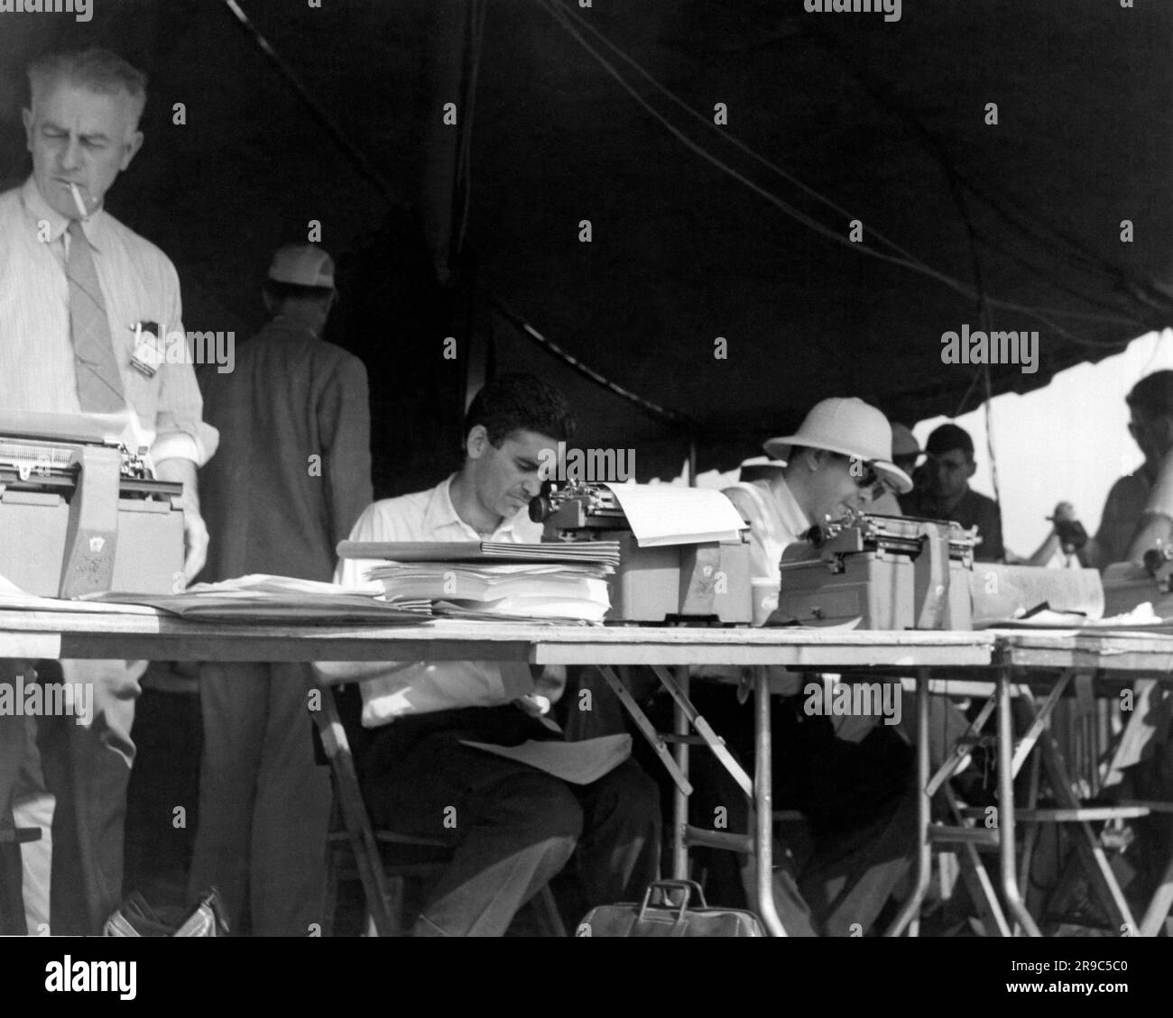 United States,  circa  1952 Reporters and journalists working in the field on typewriters on tables under a portable tent shelter. Stock Photo
