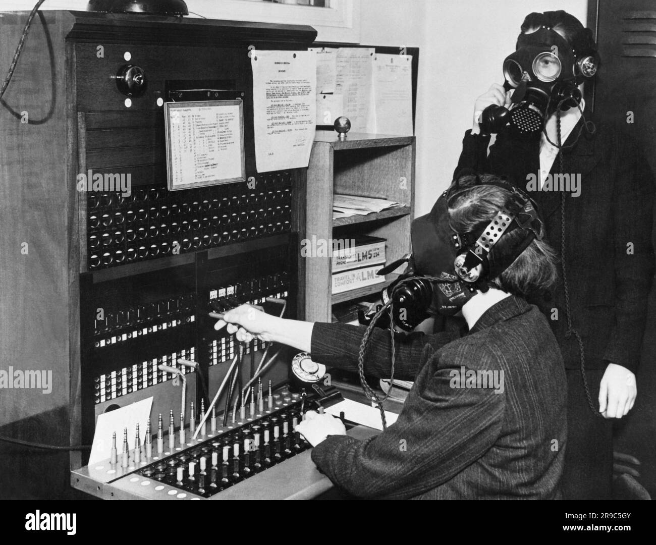 London, England:  1939 Telephone operators at Westminster Hospital wearing special gas masks with microphone attachements so that they can continue to work during German Luftwaffe air raids. Stock Photo