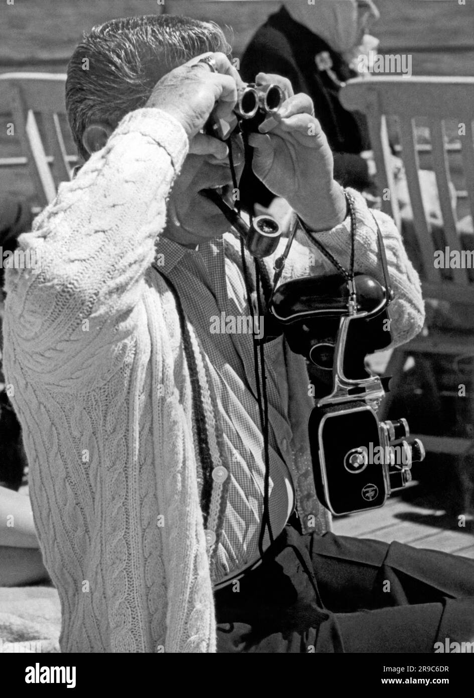 Alaska:  c. 1958. A passenger on the Canadian cruise ship, Prince George, is well prepared with two cameras, binoculars, and a pipe as they cruise through the Inside Passage from Vancouver to Skagway. Stock Photo