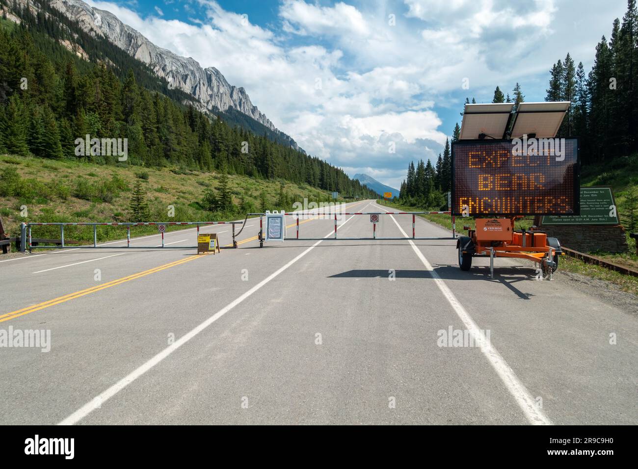 Seasonally closed Highway 40 Road Gate at Kananaskis Country Lakes Turnoff, with Alberta Parks Bear Cyclist Warning Sign on Electronic Board Stock Photo