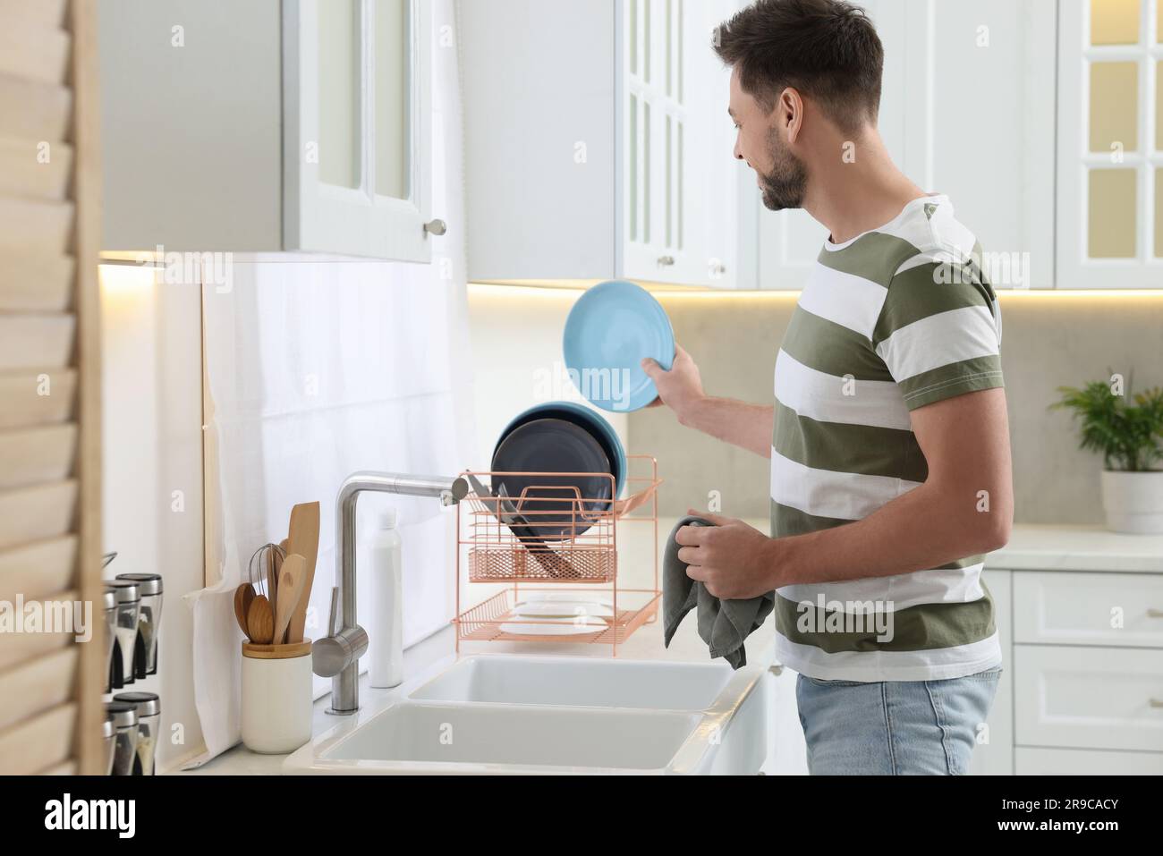Man putting clean plate on drying rack in kitchen Stock Photo