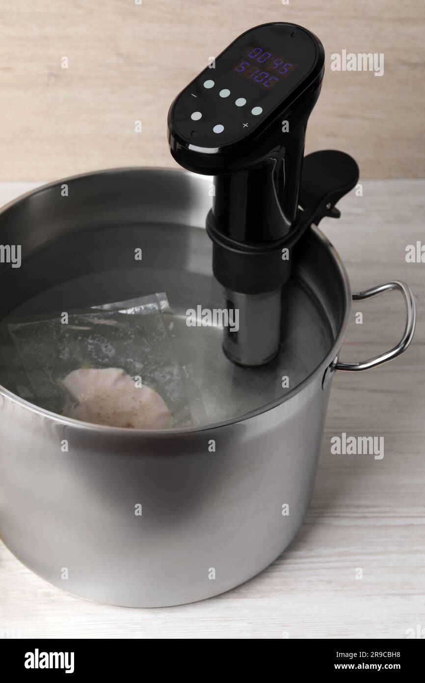 Thermal immersion circulator and vacuum packed meat in pot on white wooden table. Sous vide