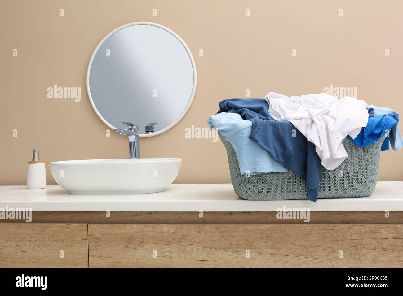 Plastic laundry basket overfilled with clothes on countertop in bathroom Stock Photo