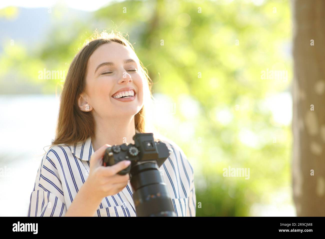 Happy photographer breathing fresh air holding camera standing in nature Stock Photo