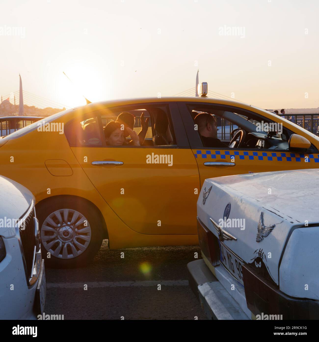People wave from a yellow taxi on Galata Bridge approaching sunset on a summers evening, Istanbul, Turkey Stock Photo