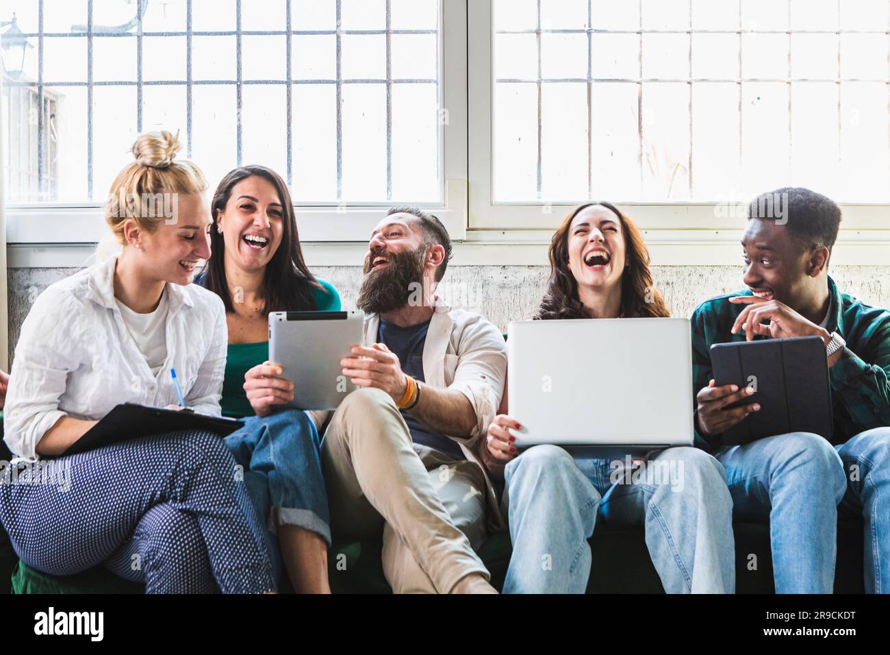 multi-ethnic group of friends bursting out laughing while watching videos on tablet, generation Z technology fun concept. Youth and multicultural dive Stock Photo