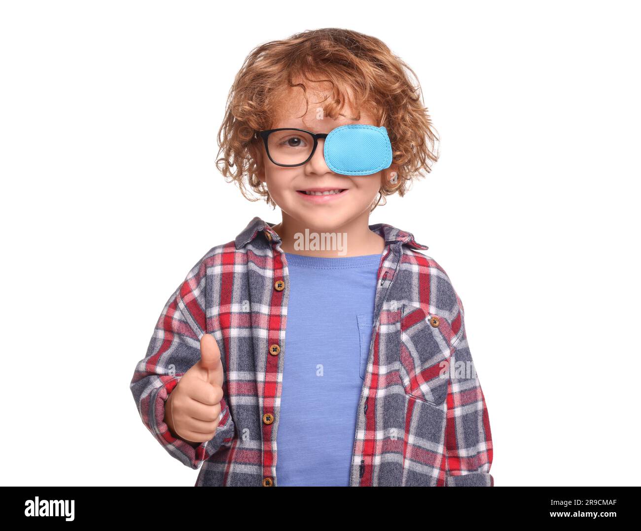 Happy boy with eye patch on glasses showing thumb up against white background. Strabismus treatment Stock Photo