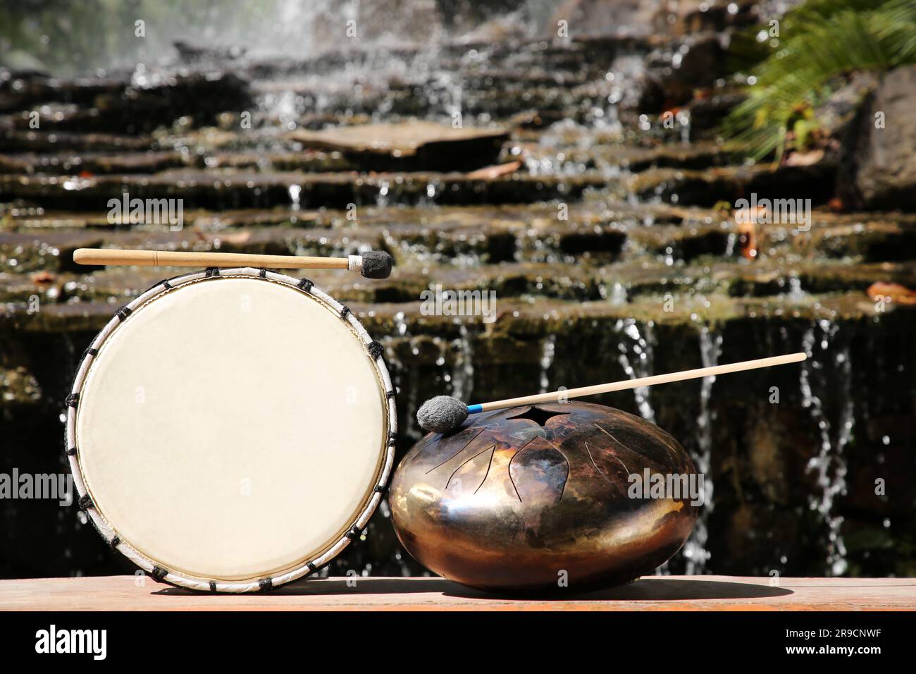Drum and handpan with mallets near waterfall outdoors on sunny day