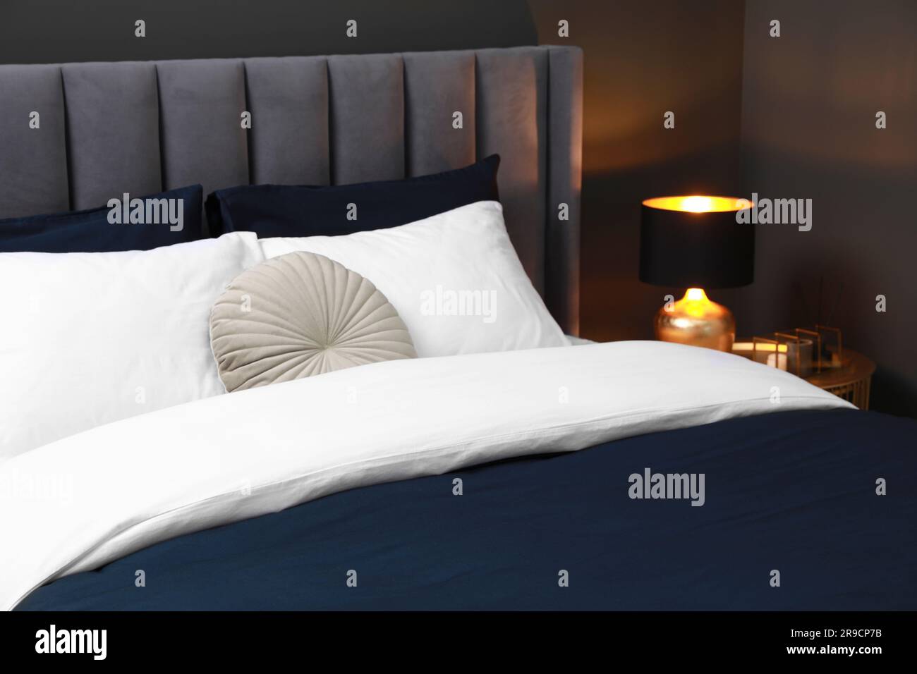 Comfortable bed with cushions, lamp and different decor on bedside table in room. Stylish interior Stock Photo