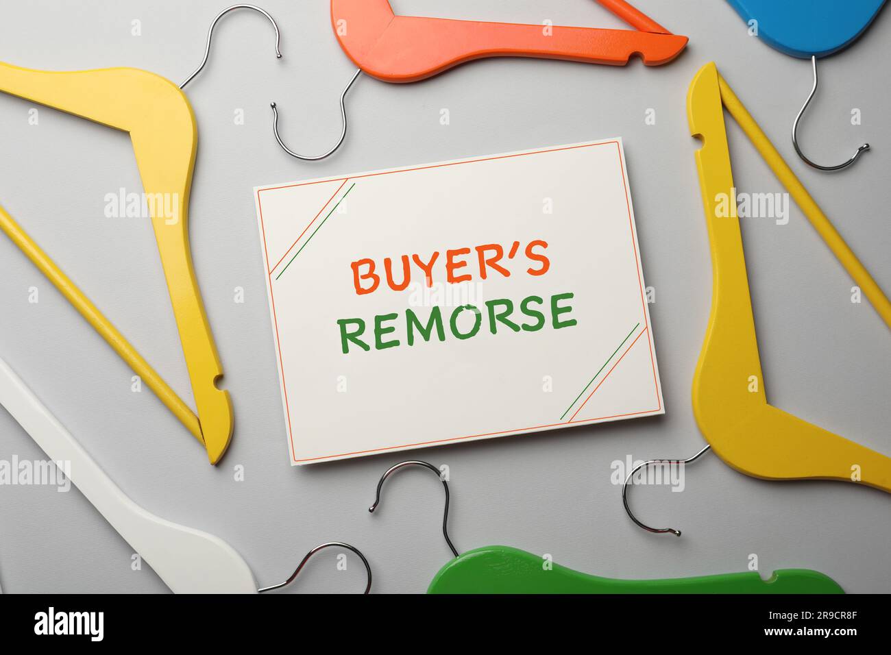 Card with text Buyer's Remorse and different colorful hangers on light grey background, flat lay Stock Photo