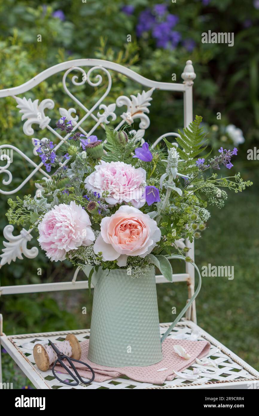 bouquet of rose, peonies and summer flowers in vintage jug on garden chair Stock Photo