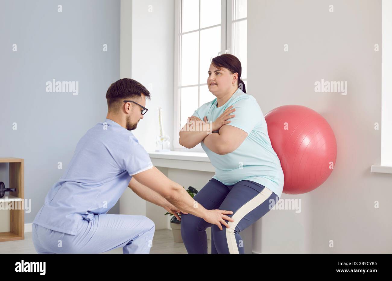 Young male nurse helping fat overweight woman doing sport exercises with fit ball. Stock Photo