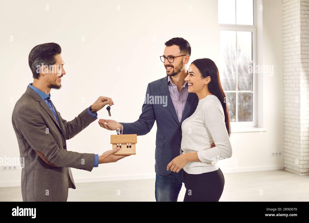 Real estate agent giving house key to a young happy smiling couple ...