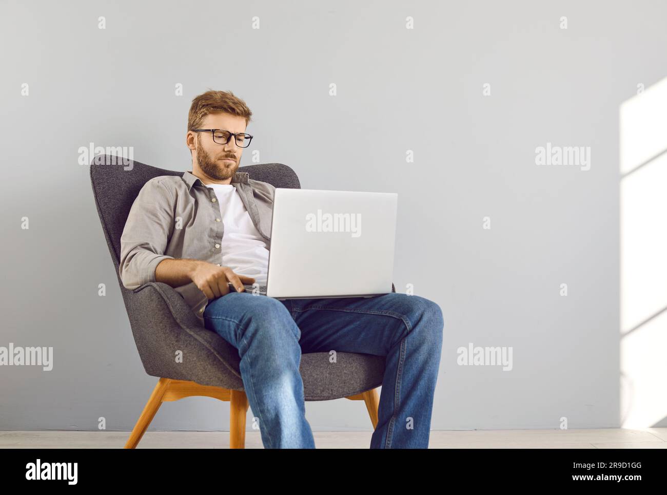 Handsome young bearded businessman sitting on chair in a empty space with laptop and working. Stock Photo