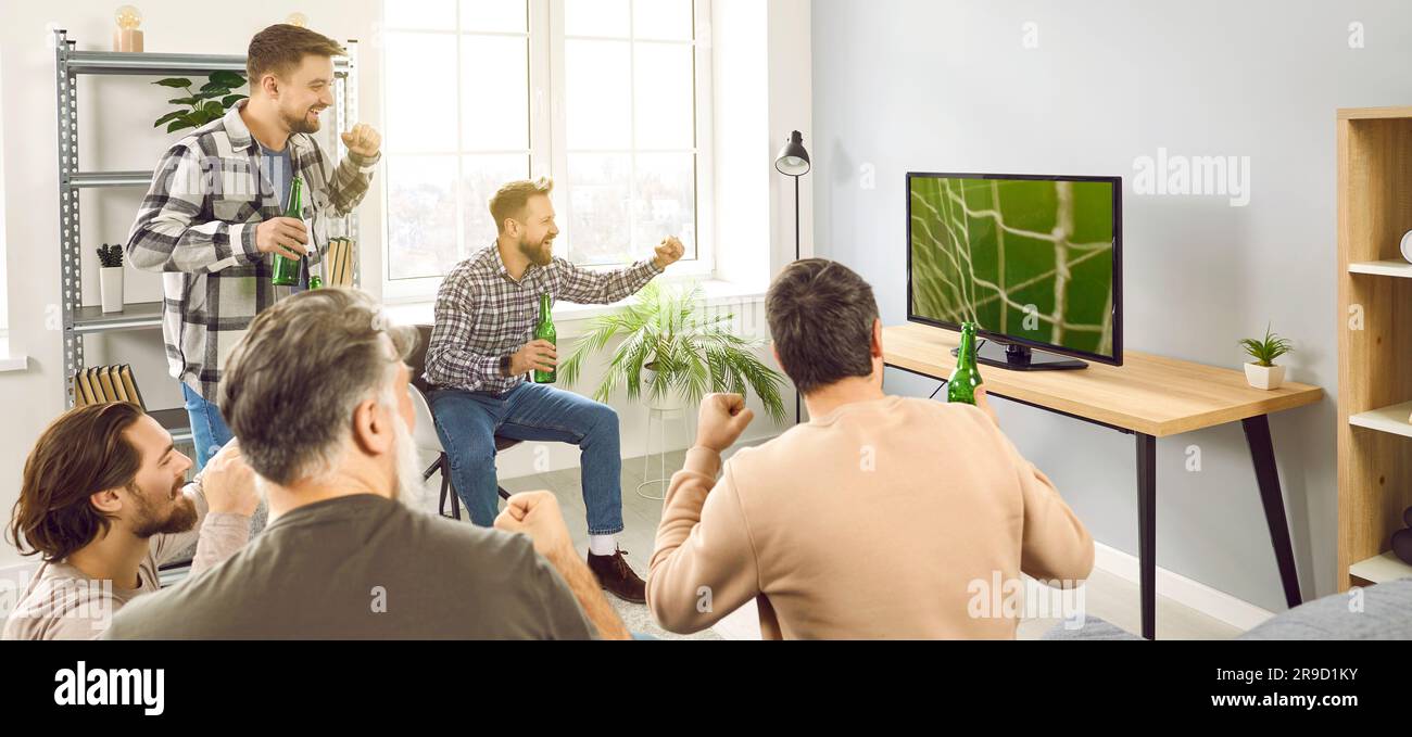 Group of male friends watching football on TV, celebrating goal, and drinking beer Stock Photo