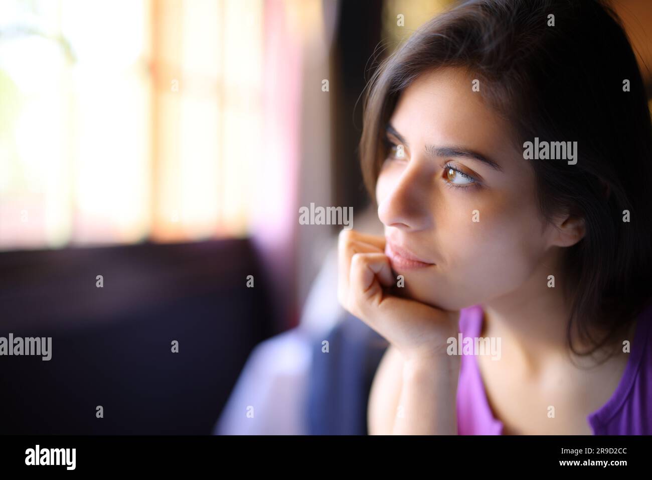 Pensive woman relaxing looking through a window sitting at home Stock Photo