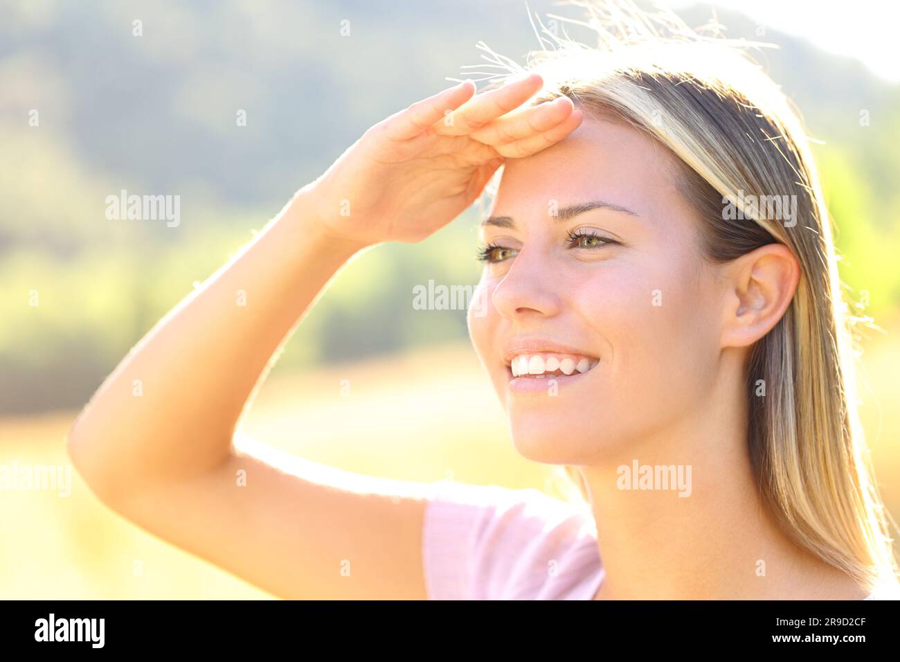 Happy woman with hand on forehead protects from sun in nature Stock Photo