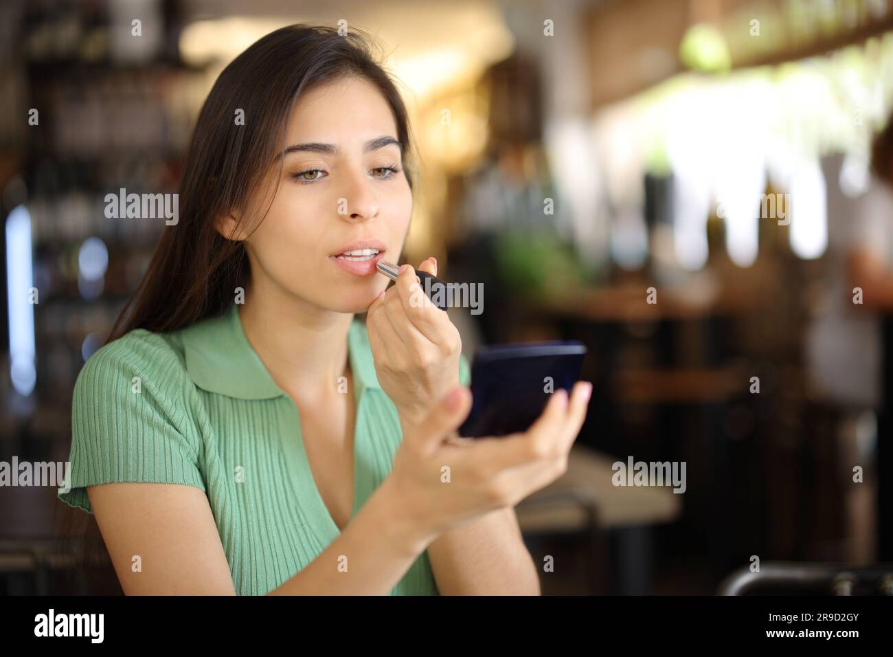 Woman painting lips before dating in a restaurant interior Stock Photo