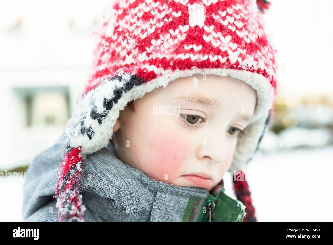 Cold boy wearing winter hat looking down while standing in the snow ...