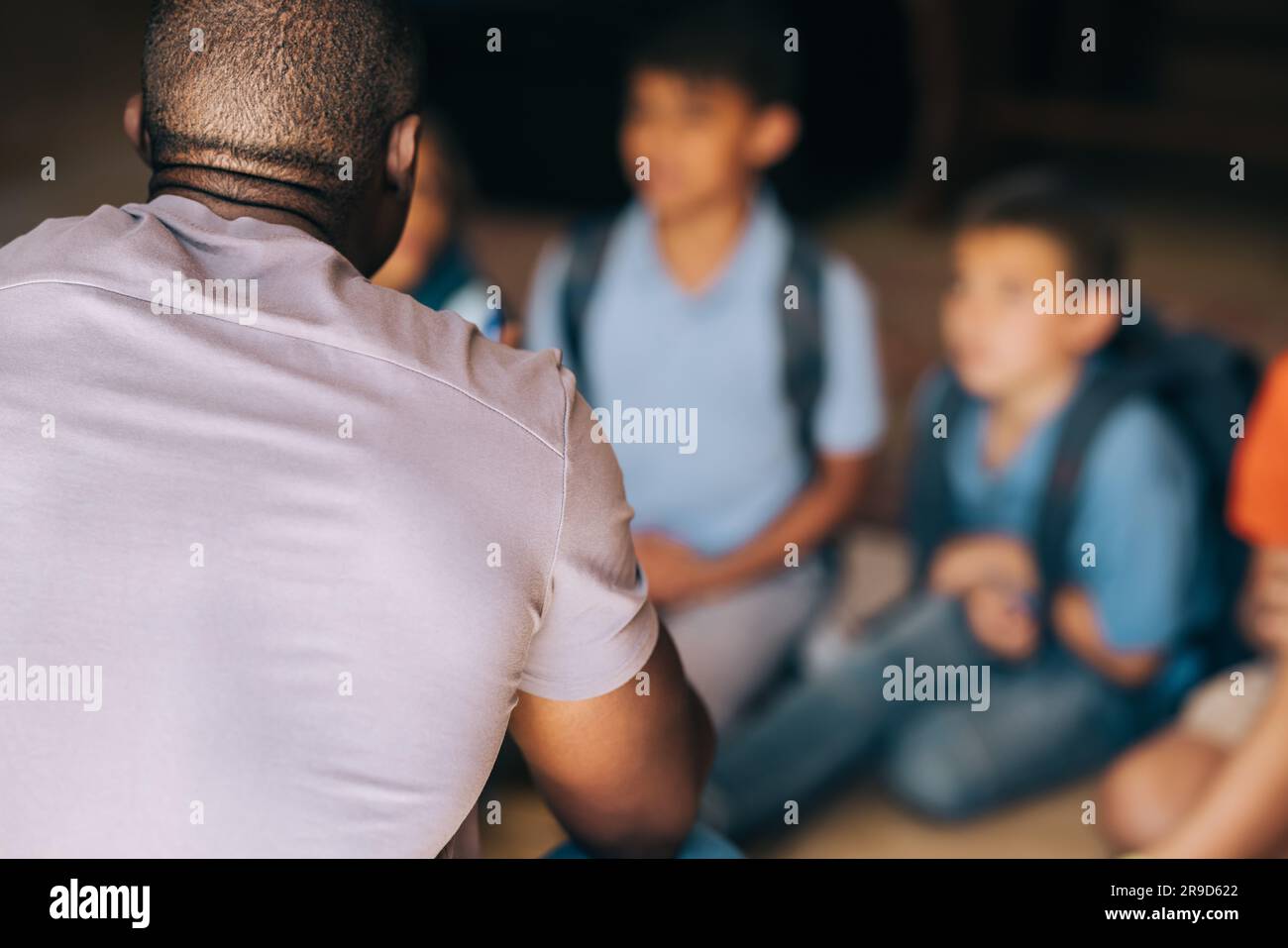 school mentor talking to a group of children in elementary school. Male teacher giving a motivational speech to his students. Primary school educator Stock Photo