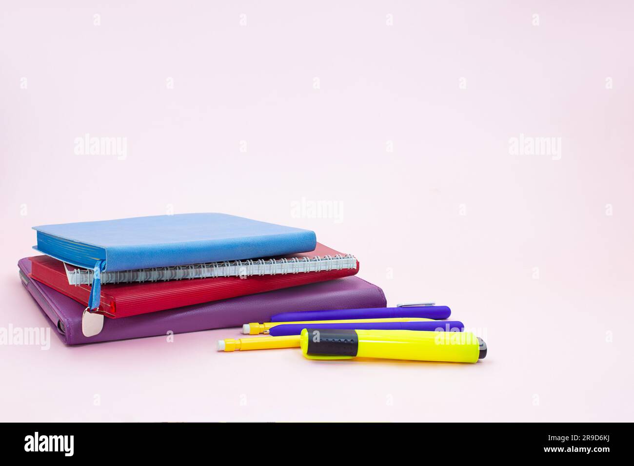 Stack of notepads with pen and marker on pink table. Back to school. Copy space Stock Photo