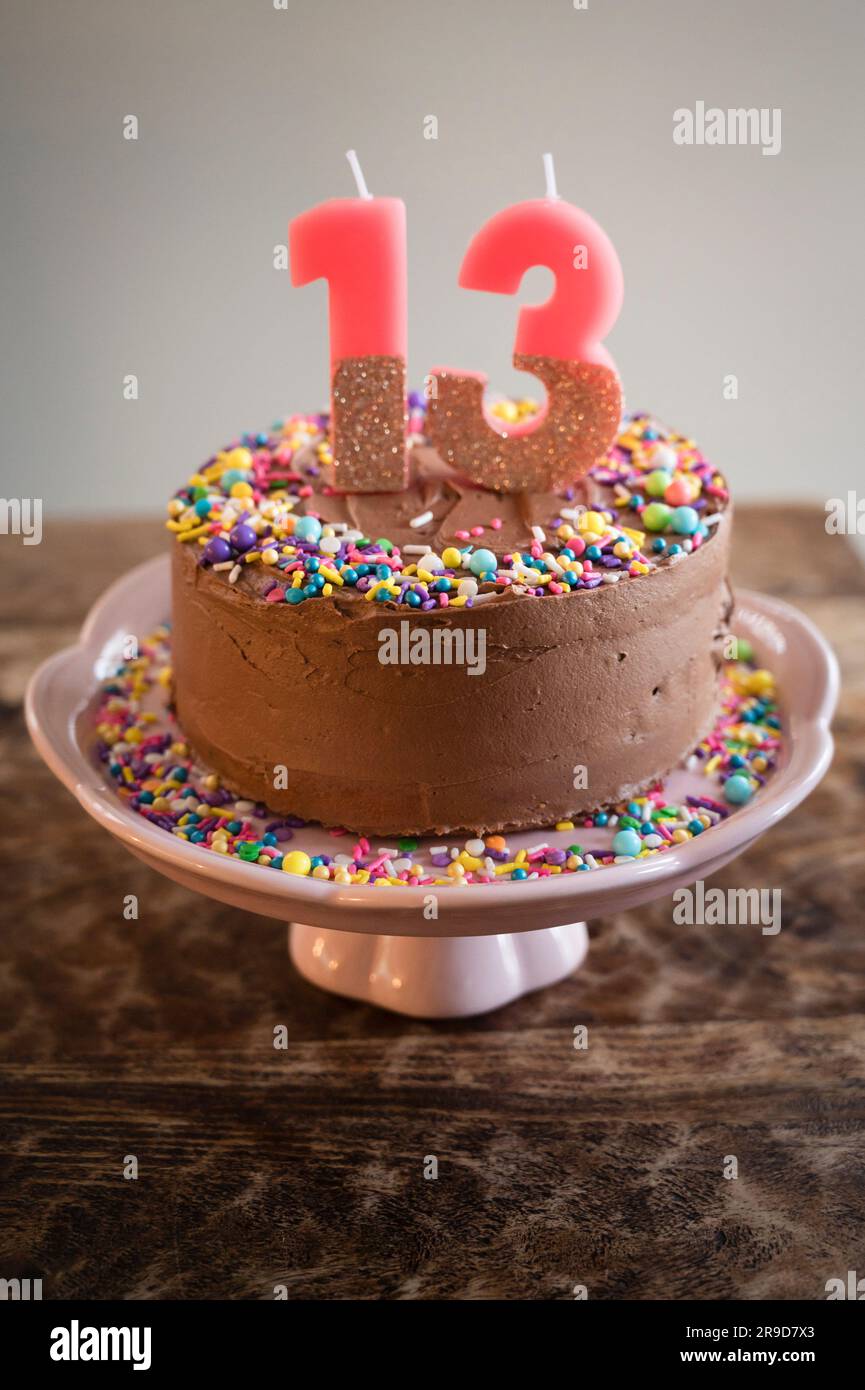 birthday Cake with Sprinkles and Candles in Shape of 13 on Table Stock Photo