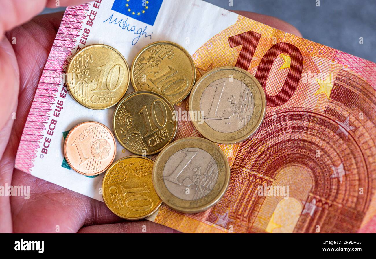 Berlin, Germany. 26th June, 2023. ILLUSTRATION - Banknotes and euro coins  with the value of 12.41 euros are on one hand. The general legal minimum  wage in Germany is to rise from