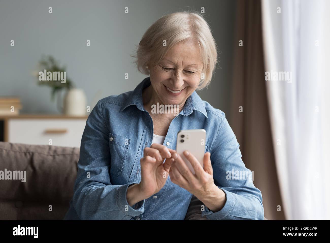 Smiling elderly woman using cell phone seated on couch Stock Photo
