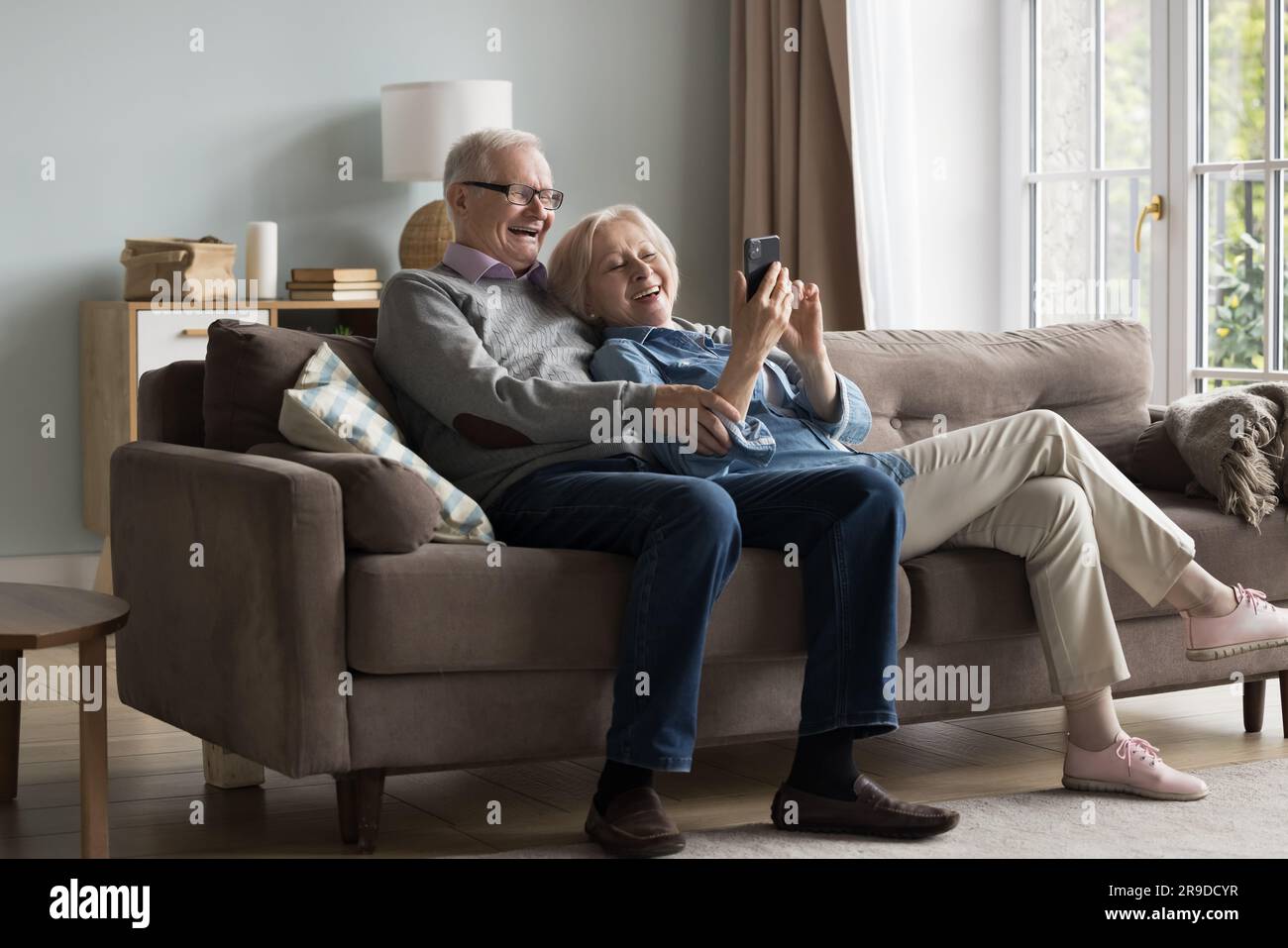 Happy mature couple using cell phone relaxing together on sofa Stock ...