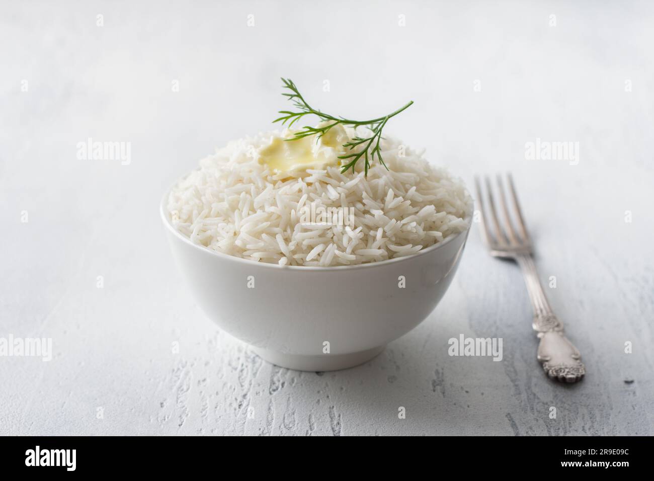 A bowl of steamed long grain rice with butter and a sprig of dill on a light gray background. Stock Photo