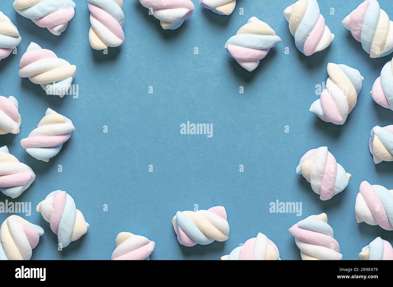 White, yellow, pink, and light blue marshmallows on blue background with copy space. Stock Photo