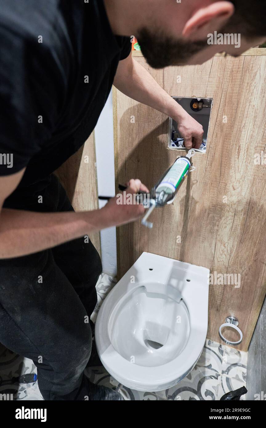Man plumber using plumbing tool applicator gun while installing toilet