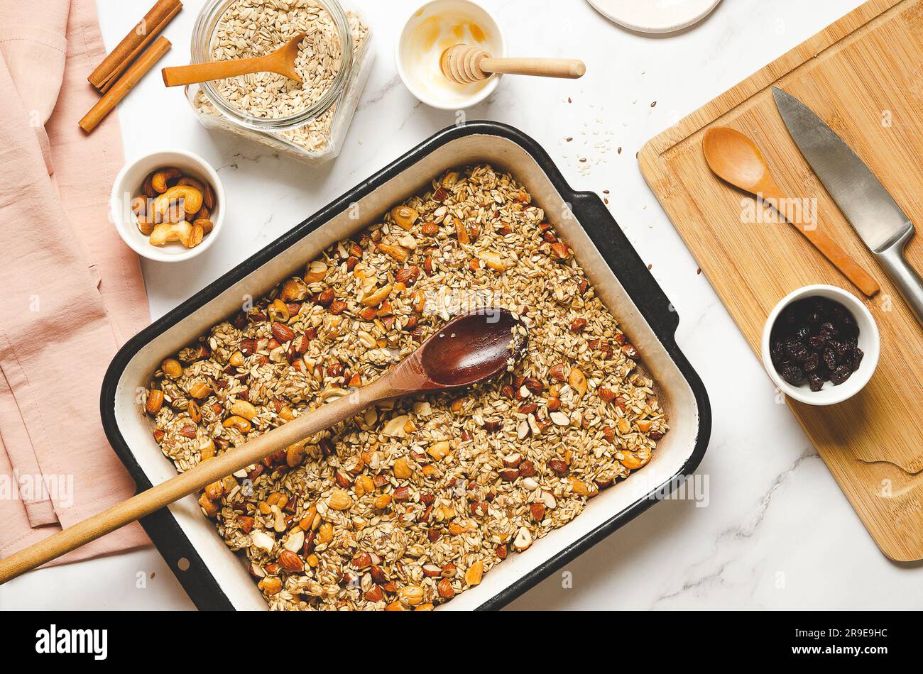Homemade granola with nuts, dried cranberries and honey in a baking pan on a white marbled background, top view. Stock Photo