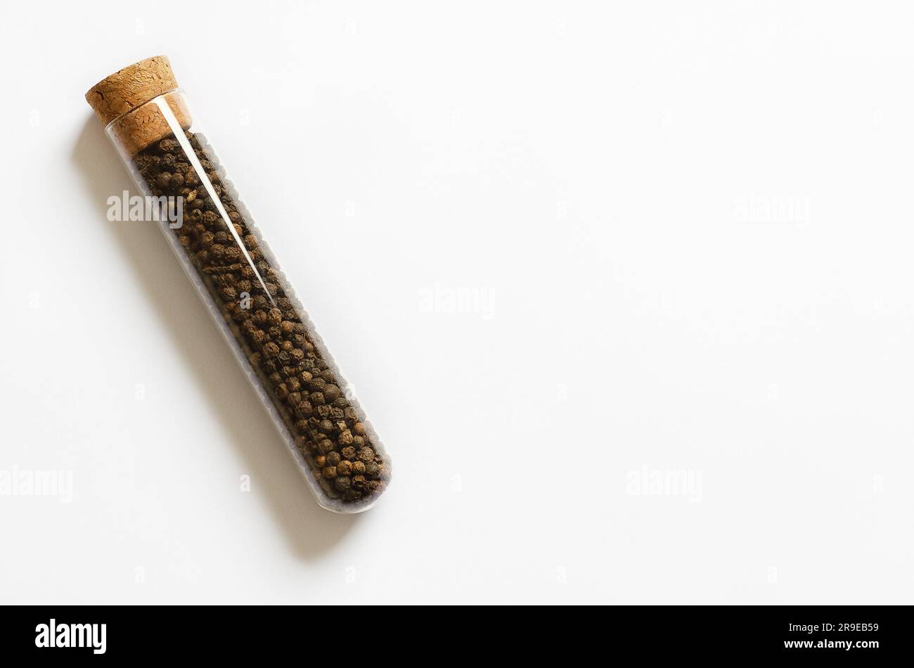 Peppercorns in a glass container on a white background with copy space