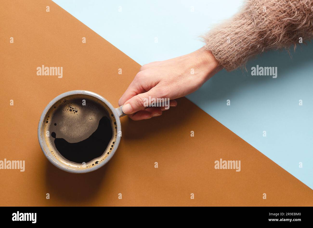 Female hand holding a cup of coffee on a blue and brown background. Stock Photo