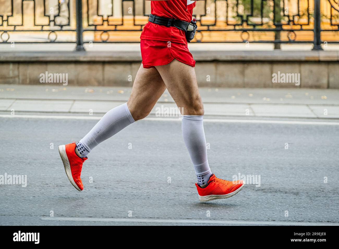 side view male runner run marathon race in white compression socks and bright red running shoes Stock Photo