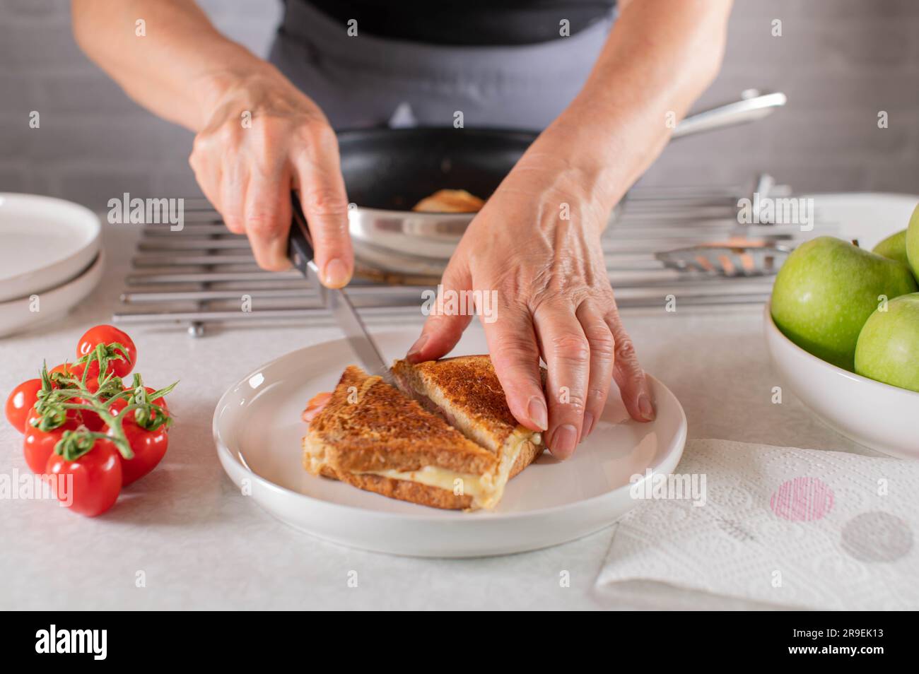 Ham and cheese sandwich is  cut in half by womans hand with a knife Stock Photo