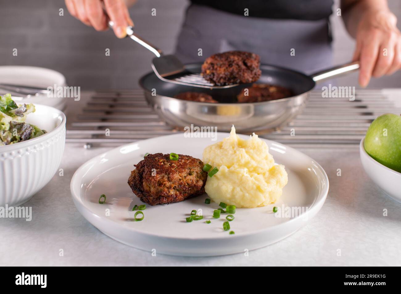Woman with apron serving meatballs from a frying pan on a plate Stock Photo