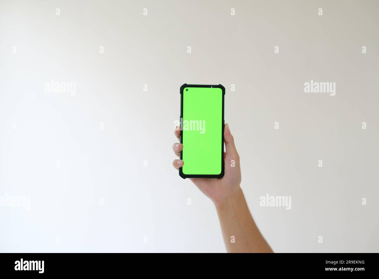 A hand is lifting up a smartphone with a green screen. Isolated white