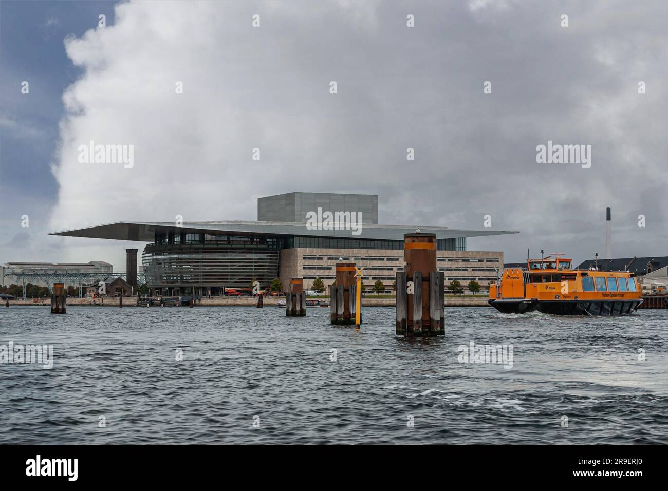 Copenhagen, Denmark - September 14, 2010: Orange Nyhavn-Opera ferry on gray water with South and west facades of Opera building under gray cloudscape Stock Photo
