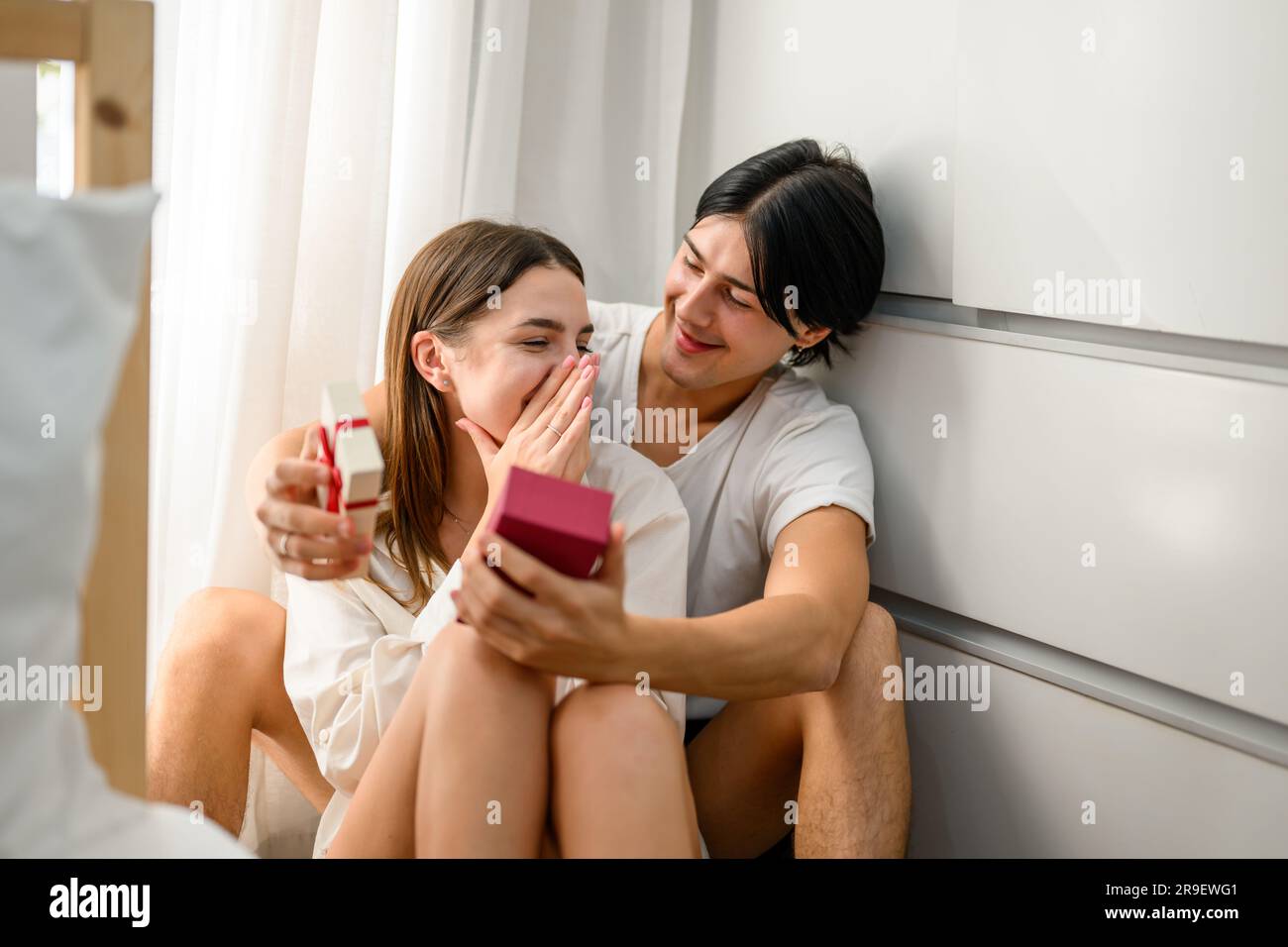 Handsome man holding small red box with gift to amazed girlfriend Stock Photo