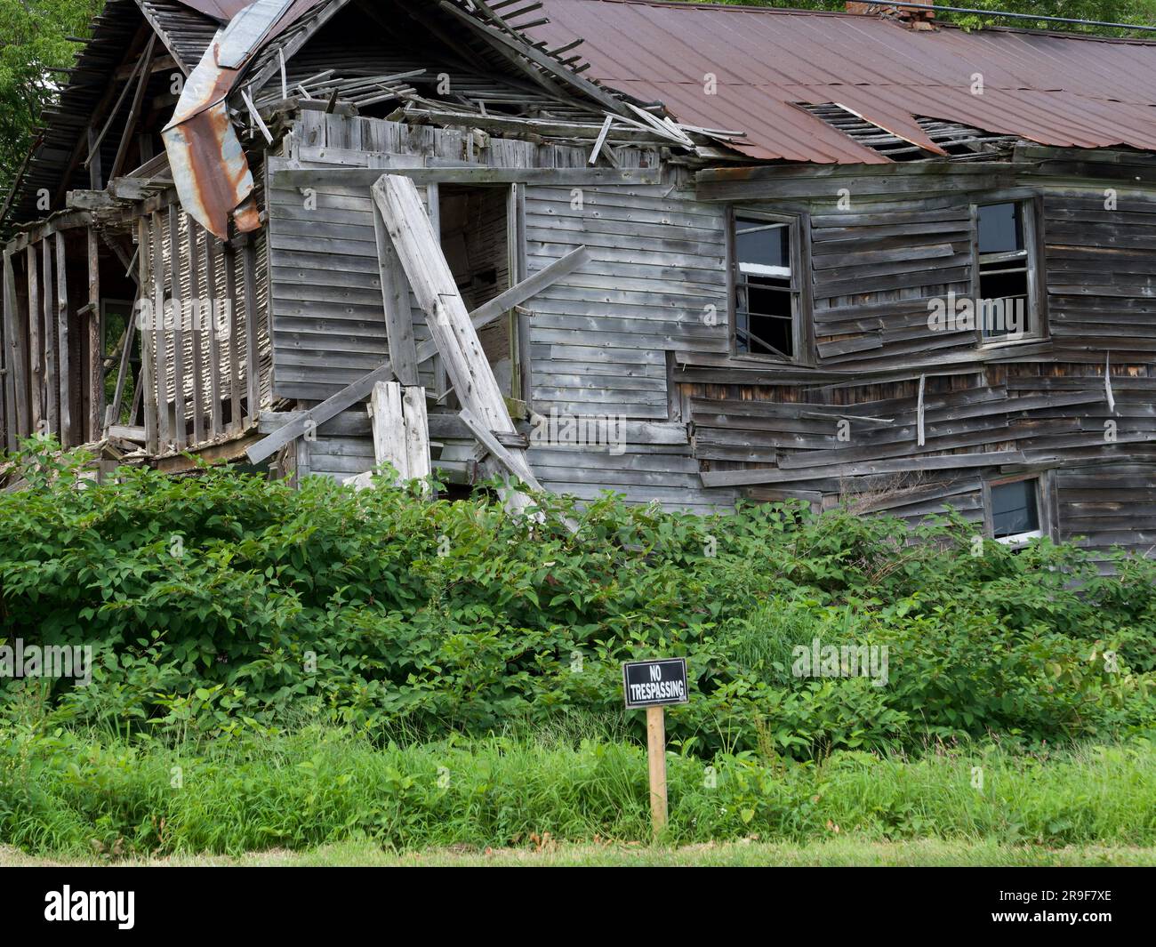 Decay and abandonment tell the story of forgotten history. A dilapidated wooden building, its collapsing structure marked with a 'No Trespassing' sign Stock Photo