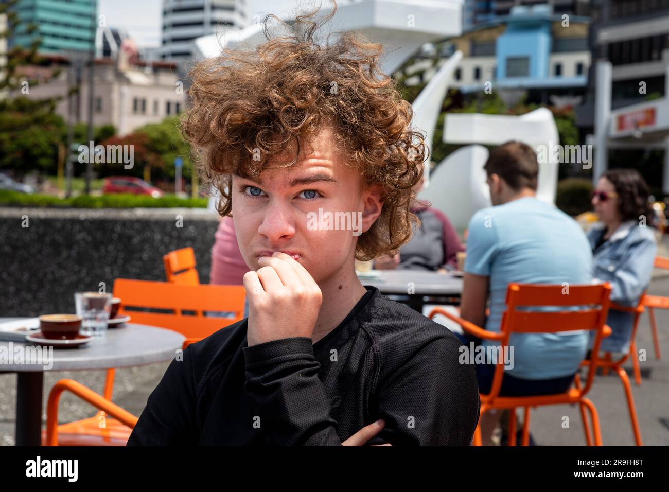 A boy with long curly hair at a cafe in Wellington, New Zealand, Capital City, Harbour, Recreation Area. Model Release available. Photo: Rob Watkins Stock Photo
